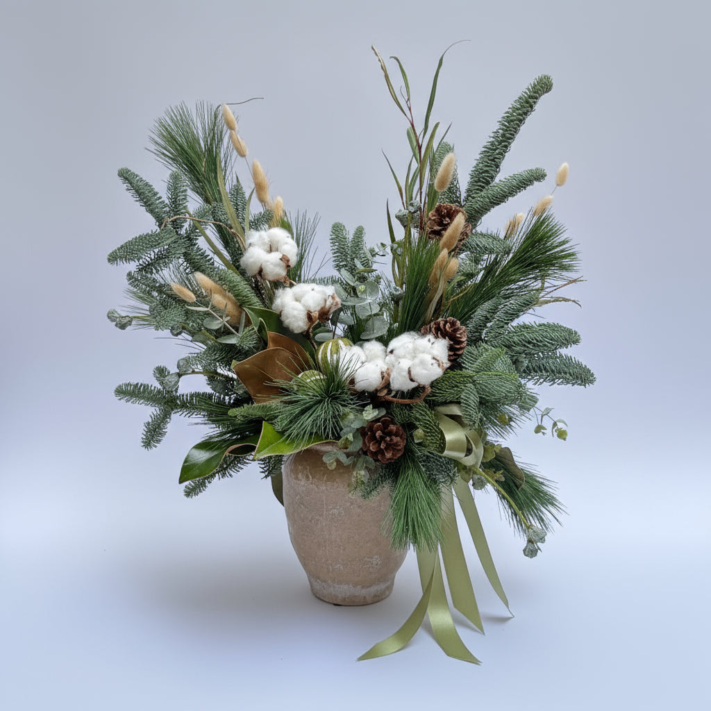 centro navideño en color blanco y verdes con abeto y pino natural, con flores de algodón y piña seca y frutos deshidratados  sobre una base beis cerámica. 
