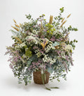 centro de flores secas con lavanda espiga y estatis en colores claros con toque de eucalipto natural sobre una base de cesta de mimbre marron, en un fondo de estudio blanco