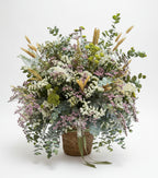 centro de flores secas con lavanda espiga y estatis en colores claros con toque de eucalipto natural sobre una base de cesta de mimbre marron, en un fondo de estudio blanco