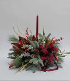 centro de mesa navideño con abeto natural y acebo natural, el centro es en colores verdes, rojos  toques de dorado. fondo neutro blanco