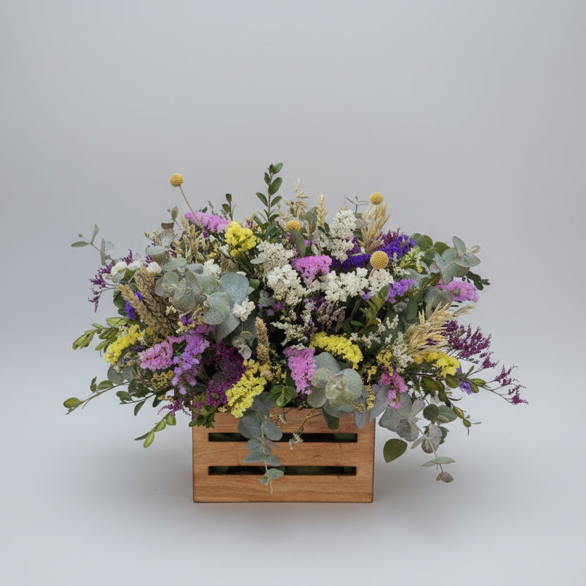 centro de flores secas colorido  sobre una caja de madera en color neutro, compuesto de estatis colorido, espiga natural y flores de campo en seco