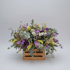 centro de flores secas colorido  sobre una caja de madera en color neutro, compuesto de estatis colorido, espiga natural y flores de campo en seco