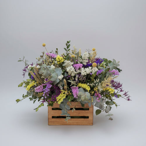 centro de flores secas colorido  sobre una caja de madera en color neutro, compuesto de estatis colorido, espiga natural y flores de campo en seco
