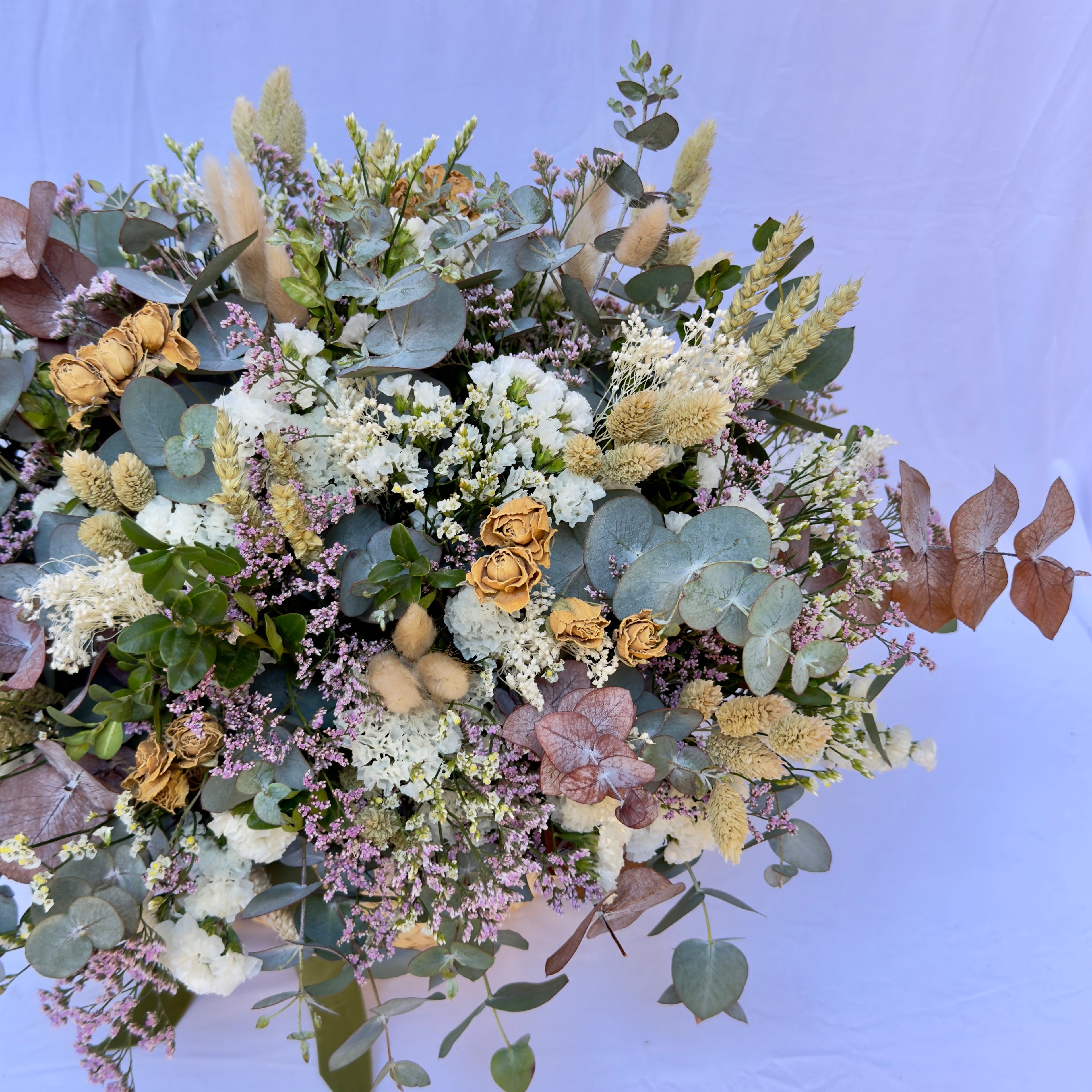 cesto de flores secas en color blancos y verdes de eucalipto y flores de campo preservadas sobre una base de mimbre beiges con cinta de terciopelo verde botella