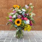 ramo de colores primaverales sobre jarrón transparente y rematado por un lazo verde de satén.