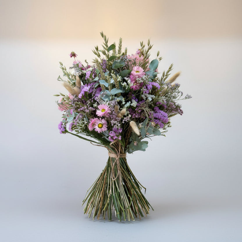 ramo de flores secas en color rosa, blancos y verdes, compuesto por flores de siemprevivas, limonium y toques de espiga y cebada natural con flores de campo en seco. el ramo está atado con una cuerda de yute marrón con sus tallos limpios. toda la imagen está sobre un fondo blanco en luz neutra.