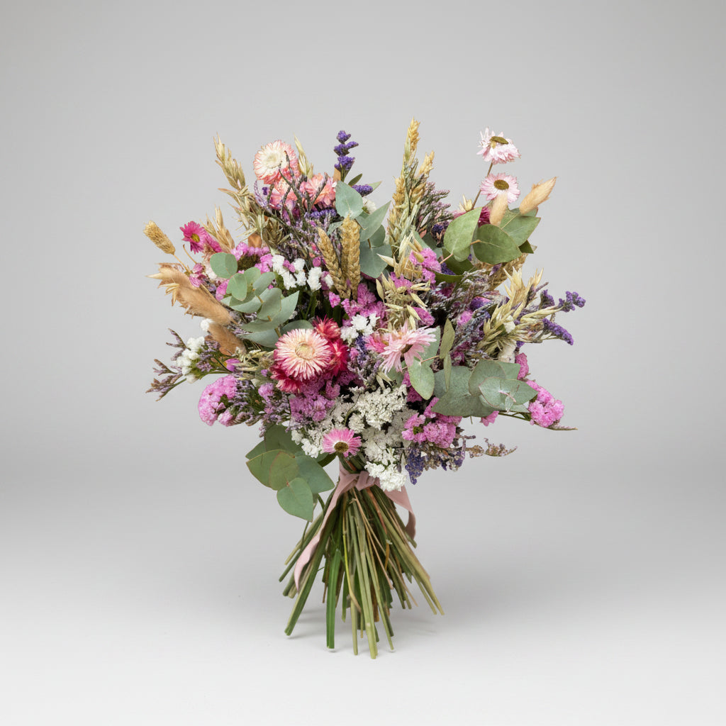 ramo de flores secas en color rosa, blancos y verdes, compuesto por flores de siemprevivas, limonium y toques de espiga y cebada natural con flores de campo en seco. el ramo está atado con una cuerda de yute marrón con sus tallos limpios. toda la imagen está sobre un fondo blanco en luz neutra.