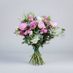 ramo de peonias rosas y flores como rosa y crisantemo en los mismos tonos y verdes naturales atado con una cinta de color verde sobre un fondo gris claro y luz neutra