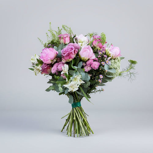 ramo de peonias rosas y flores como rosa y crisantemo en los mismos tonos y verdes naturales atado con una cinta de color verde sobre un fondo gris claro y luz neutra