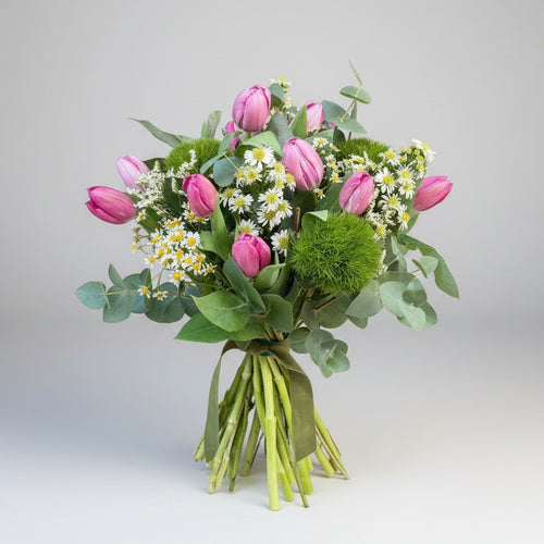 ramo de tulipanes en color rosa con toques de manzanilla y verdes naturales atado con una cinta de terciopelo verde en un fondo blanco gris claro con luz neutra